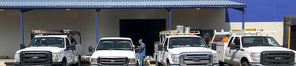Four white Ice & Fire Mechanical service pickups lined up outside the shop