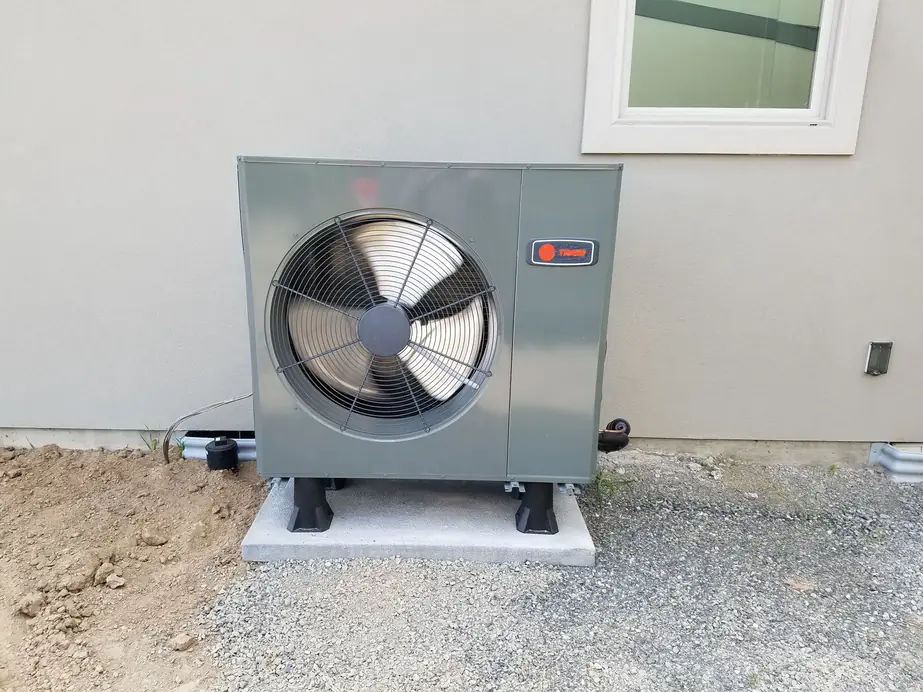 New Trane heat pump condenser on a fresh concrete pad against grey stucco