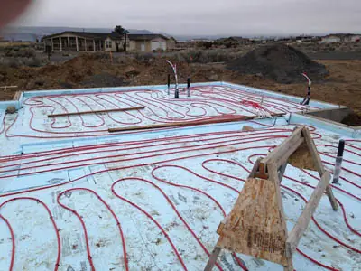 Red PEX radiant heating loops stapled across foam board on a new concrete slab